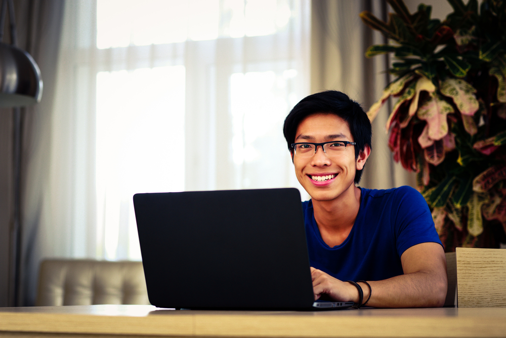 Happy asian man sitting at the table with laptop